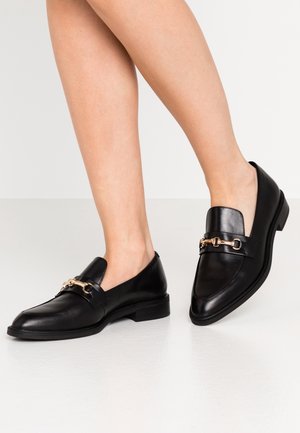 Black leather loafers with a rounded toe, featuring a gold chain detail across the vamp, and a low stacked heel. Smooth texture.
