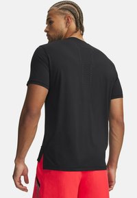 Camiseta negra de manga corta con una textura suave, con pequeñas perforaciones a lo largo de la espalda, combinada con pantalones cortos de color rojo brillante.