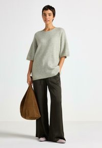 Maglione oversized grigio chiaro a maglia, con maniche corte, abbinato a pantaloni larghi verde scuro e una borsa slouchy in suede marrone.