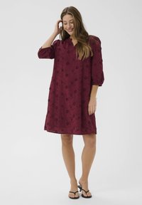 Burgundy klänning med V-ringning, trekvarts puffärmar, blommönstrad prägling och A-linjeform, matchad med svarta flip-flops.