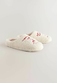 Krémovobiele papuče na nosenie bez zapínania, vyrobené z nadýchaného materiálu s červeným vyšívaným nápisom a kvetinovými vzormi na hornom povrchu.
