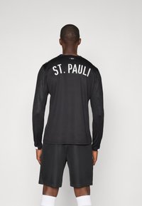 Czarna sportowa koszulka z długim rękawem z białym napisem "ST. PAULI" z tyłu. Połączona z dopasowanymi szarymi szortami. Brak widocznych wzorów.