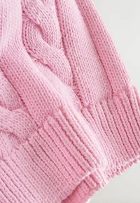 Rožinis megztinis, pagamintas iš megztos tekstūruoto kabelio rašto ir su ribiniais rankogaliais. Minkšta, stora siūlė su lygiu dygsnio raštu.