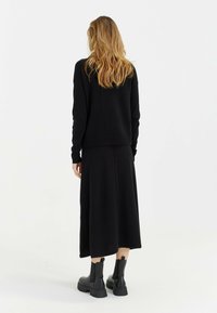 Zwarte trui en lange rok van gebreid materiaal, met een relaxte pasvorm. Zwarte enkellaarzen met een chunky zool maken de outfit af.