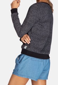 Suéter negro con puntos, de mangas largas y dobladillo acanalado negro, combinado con pantalones cortos de color azul claro con bolsillos laterales.