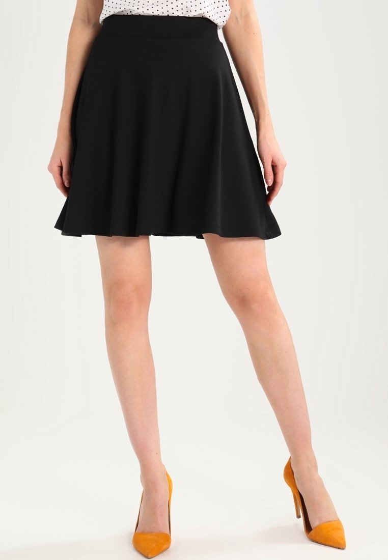 Schwarzer, aus glattem Stoff gefertigter, ausgestellter Rock, der eine taillierte Passform hat und bis zum Knie fällt. Kombiniert mit spitz zulaufenden, orangefarbenen High Heels.