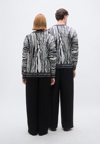 Pull en maille noir et blanc à motif ondulé, associé à un pantalon noir à jambes larges. Poignets visibles et détails de col structuré.