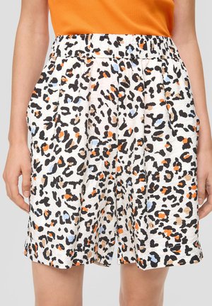 Hvide shorts med sort, orange, beige og lyseblåt leopardmønster, båret med en orange top, hænder afslappet langs siden.