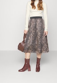A midi pleated skirt with a brown and beige abstract pattern, paired with a fitted cream turtleneck and brown ankle boots with a heel.