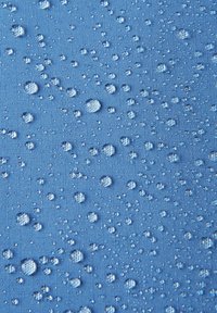 Superficie di tessuto blu coperta di gocce d'acqua, di dimensioni variabili, con una trama texturizzata visibile sotto l'umidità.