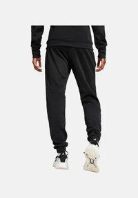 Schwarze athletische Jogginghosen mit schmalem Schnitt, strukturiertem Stoff und kontrastierenden Nahtdetails, kombiniert mit schwarz-weißen Sneakers.