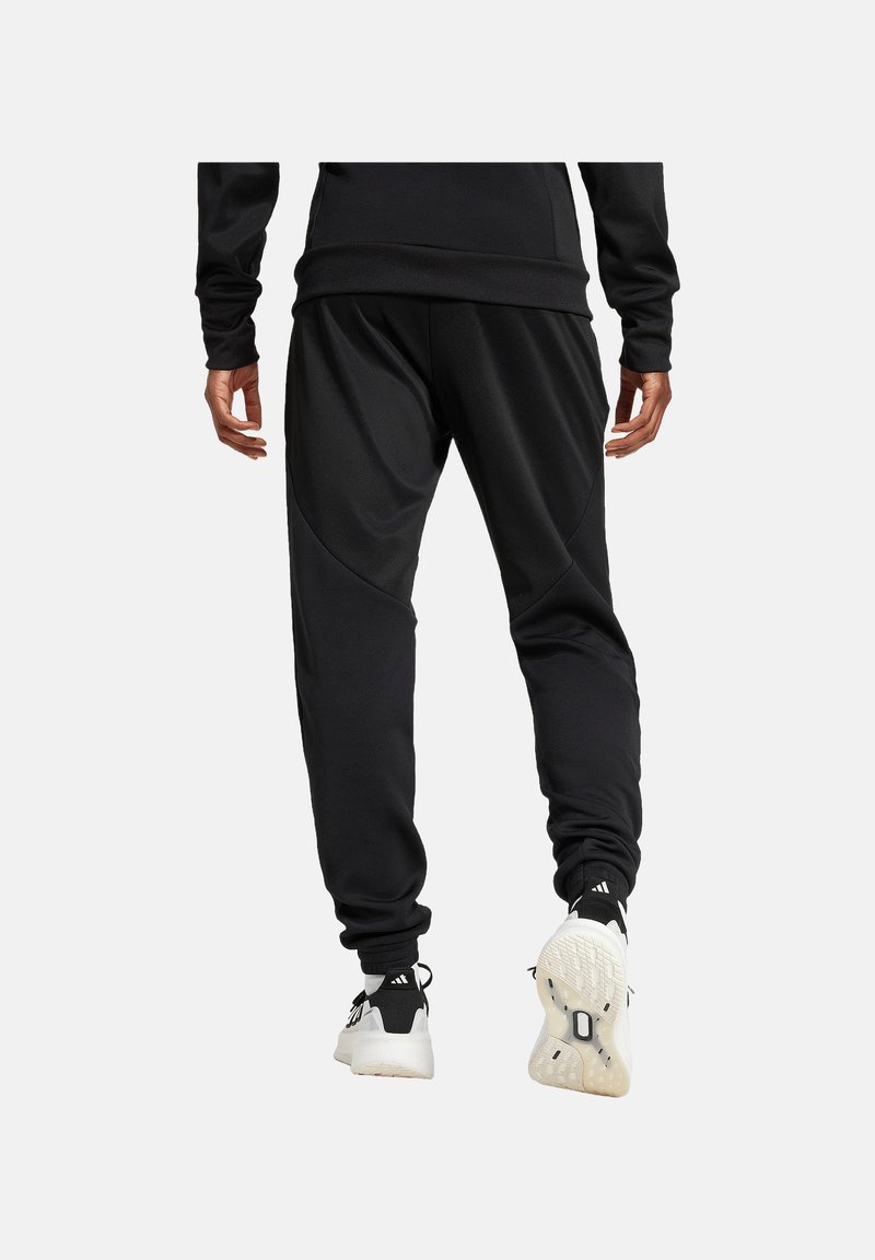 Schwarze athletische Jogginghosen mit schmalem Schnitt, strukturiertem Stoff und kontrastierenden Nahtdetails, kombiniert mit schwarz-weißen Sneakers.