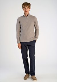 Hellbrauner Strick-Half-Zip-Pullover, marineblaue Hose und beigefarbene Slipper. Glatte Textur, körpernahe Passform und lässiger Stil.