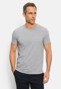 T-shirt grigio a maniche corte realizzato in cotone, con colletto rotondo e una texture liscia, indossato con pantaloni scuri. Nessun motivo o grafica visibile.
