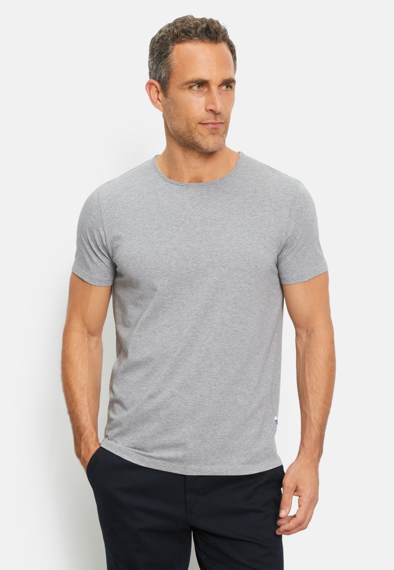 T-shirt grigio a maniche corte realizzato in cotone, con colletto rotondo e una texture liscia, indossato con pantaloni scuri. Nessun motivo o grafica visibile.