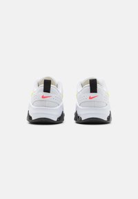 Zapatos deportivos blancos con acentos en negro y rosa, que cuentan con un cuello acolchado, parte superior de malla y una suela gruesa negra con agarre texturizado.