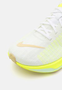Gros plan d'une chaussure de course Nike blanche avec un logo swoosh beige et des accents jaune fluo sur la semelle et les côtés.