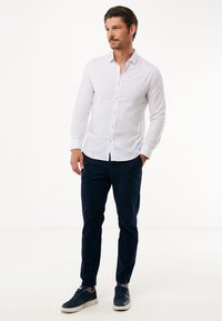 Vit långärmad skjorta med knäppning, marinblå chinos och mörkblå sneakers. Slät tyg, skräddarsydd passform och inga synliga mönster.