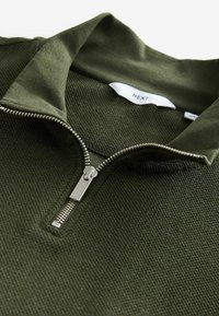 Grüner Reißverschluss-Pullover aus strukturiertem Material, mit einem Stehkragen und einem silbernen Reißverschluss. Etikett sichtbar im Kragen.