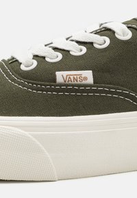 Zapatillas Vans de lona verde con cordones blancos, costuras blancas, suela de goma y etiqueta con el logotipo de Vans en el lateral.