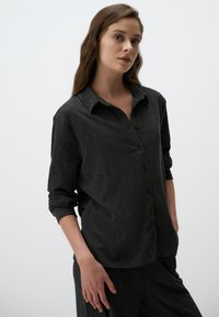 Zwarte button-up overhemd met een gestructureerd, geribbeld patroon, voorzien van een kraag en lange mouwen die tot de ellebogen zijn opgerold. Eenvoudig en eigentijds ontwerp.