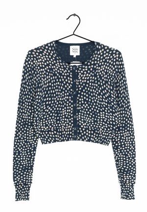 Cardigan court bleu marine avec motif de points blancs irréguliers, manches longues, col rond et fermeture par boutons, accroché sur un cintre noir.