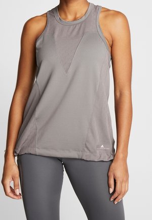 Mujer con camiseta deportiva gris sin mangas y leggings grises a juego, de pie con los brazos relajados a los lados.