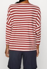 Maglietta a righe rosse e bianche a maniche lunghe con vestibilità ampia e scollatura rotonda, abbinata a pantaloni corti blu navy. Tessuto liscio, design casual.