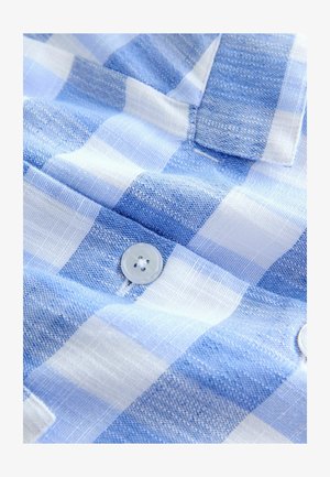 Közelkép kék-fehér kockás szövetről, texturált szövéssel és a szövetre varrt fehér gombbal.