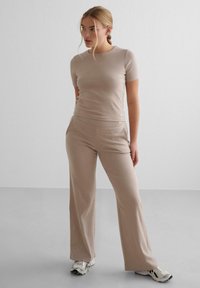 Beige fitted kortærmet top parret med matchende flagrende bukser. Glat tekstur, enkelt design og minimalistiske accenter. Fodtøj: sporty sneakers.