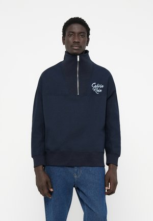 Navy zip-up sweatshirt in soft fabric with a high collar. Features a contrast logo on the chest and ribbed cuffs and hem.