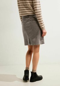 Grå corduroy nederdel med en rygsprække, parret med sorte ankelstøvler og en beige stribet sweater. Synlige baglommer og syningsdetaljer.