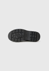 Black rubber sneaker outsole with a textured tread pattern. Features an embossed logo and a rounded heel. Durable and designed for grip.