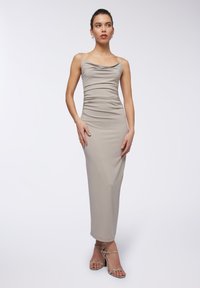 Abito midi aderente con collo a cowl in tessuto beige chiaro e dettagli arricciati. Il modello indossa sandali con tacco, aperti sulla punta, in stampa rettile.