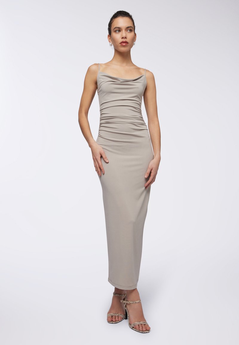 Abito midi aderente con collo a cowl in tessuto beige chiaro e dettagli arricciati. Il modello indossa sandali con tacco, aperti sulla punta, in stampa rettile.