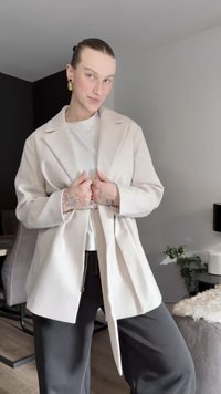 Beiger Oversize-Mantel mit breitem Revers und Gürtel, ausgestattet mit langen Ärmeln und einer glatten Textur, kombiniert mit dunkler Hose.