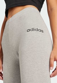 Szürke edzőnadrág puha pamut keverékből, testhez simuló kialakítással és fekete "adidas" logóval az oldalon.