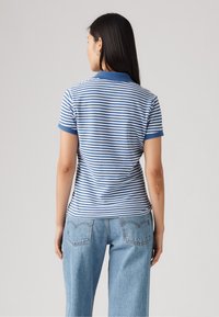 Πόλο μπλούζα κοντό μανίκι σε μπλε και άσπρες ρίγες, με σταθερό μπλε γιακά και μανίκια, συνδυασμένη με ανοιχτό μπλε ψηλού μέσου τζιν.