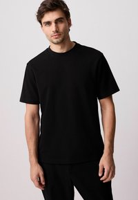 Zwarte katoenen T-shirt met een klassieke ronde hals, korte mouwen en een losse pasvorm. Gladde textuur zonder zichtbare patronen of accenten.