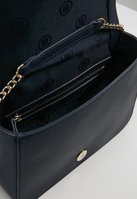 Bolso de mano de imitación de cuero azul marino con cadena, que presenta una textura suave, compartimento con cremallera y un patrón interior grabado.