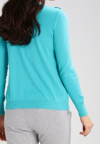 Turquoise knit sweater with a ribbed hem and cuff, featuring a smooth texture. The back view shows a simple, classic design.