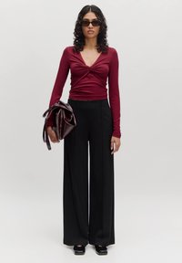 Bordeaux lange mouw top met een gedraaide voorkant, gecombineerd met hoge zwarte wijde broek; met een glanzende bordeaux tas.