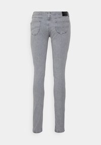 Jeans skinny de mezclilla gris con cinturilla, dos bolsillos traseros con costuras sutiles y un parche de cuero en la parte posterior de la cintura.