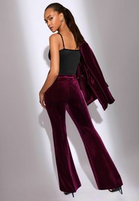 Lila bársonyos bővülő nadrág, fekete testhezálló toppal és egy azonos színű blézerral párosítva. Simaság jellemzi, finom fényességgel és precíz szabással.