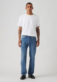 White cotton T-shirt with a crew neck, paired with straight-leg blue denim jeans. The jeans feature a classic five-pocket design.