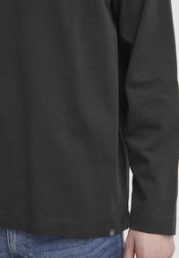 Black long-sleeve shirt made of soft cotton fabric, featuring a straight hem and a small logo tag near the bottom right seam.