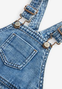 Lette blå denimoveraller med justerbare stropper, bronze hardware og en brystlomme med kontraststing.