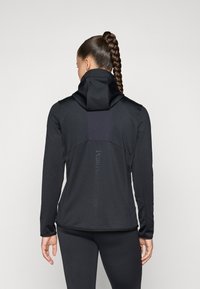 Black athletic jacket with a high collar, smooth texture, and a contrasting fabric panel on the back featuring a logo in vertical alignment.