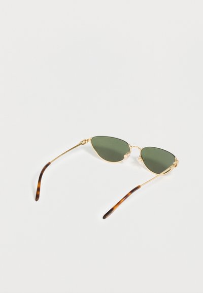 Γυναικεία γυαλιά ηλίου Cat-eye με χρυσό πλαίσιο, πράσινους φακούς και λεπτομέρειες στα ακροβραχιόνια με μοτίβο καβουροκαλύμματος σε λευκή επιφάνεια.