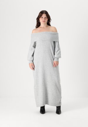 Light gray off-the-shoulder sweater dress with ribbed neckline and cuffs, long sleeves, and straight silhouette, paired with black ankle boots.